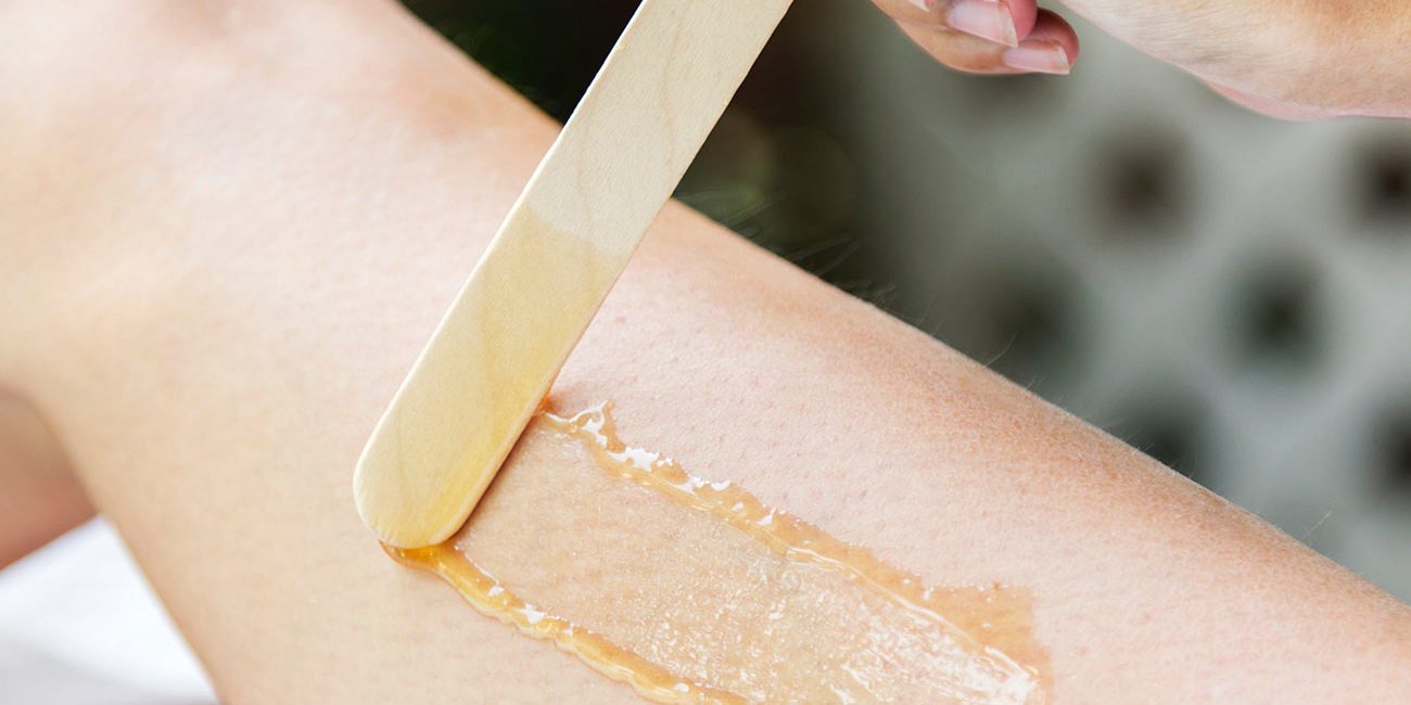 A person is waxing their leg with a wooden spatula.