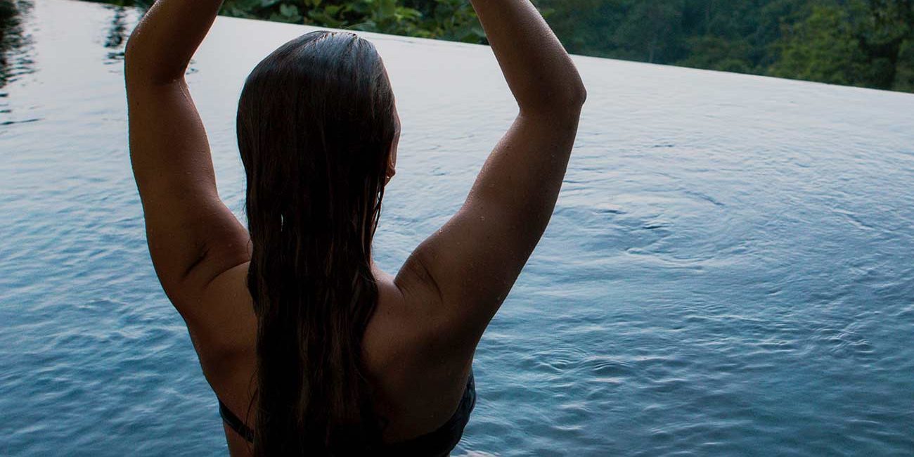 A woman sitting in the middle of a pool with her arms raised.