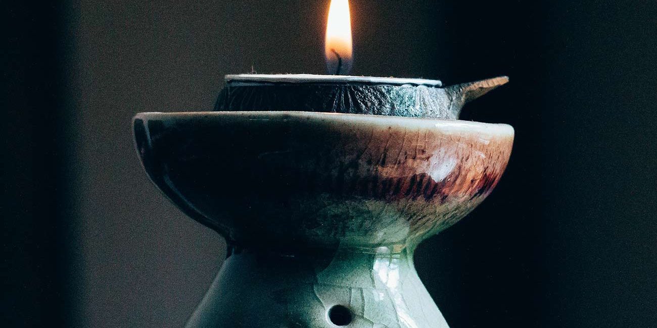 A candle in a green vase with a black background