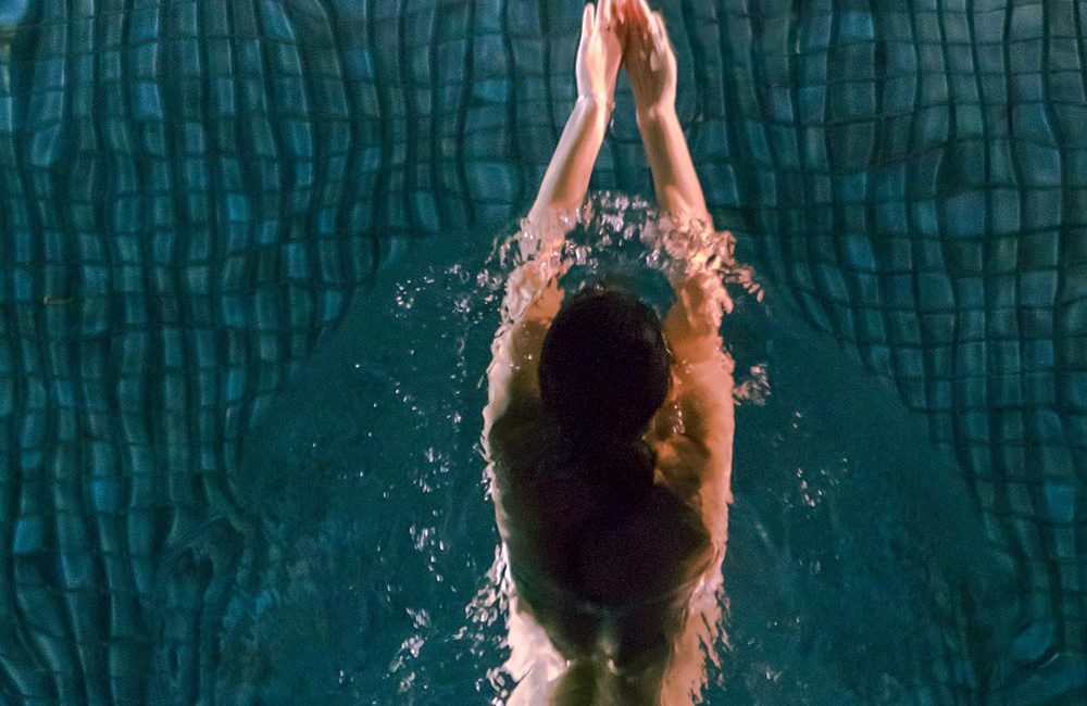 A man diving into the water in front of a pool.