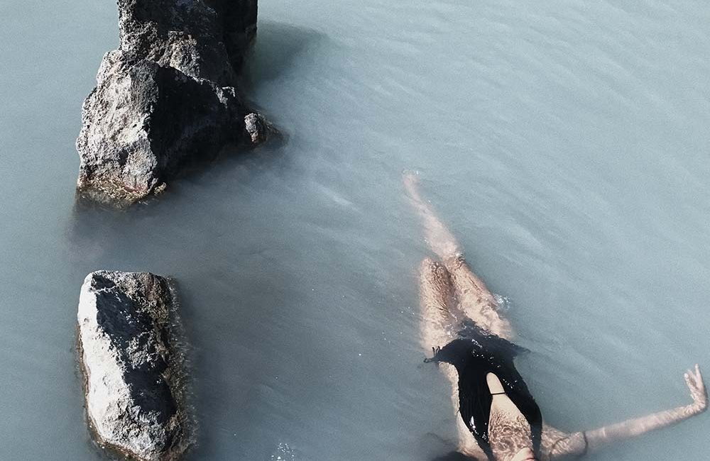 A woman floating in the water with rocks.