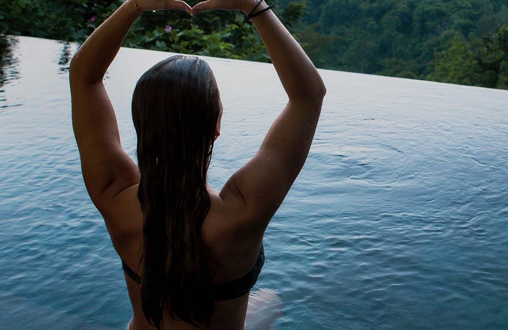 A woman sitting in the middle of a pool with her arms raised.