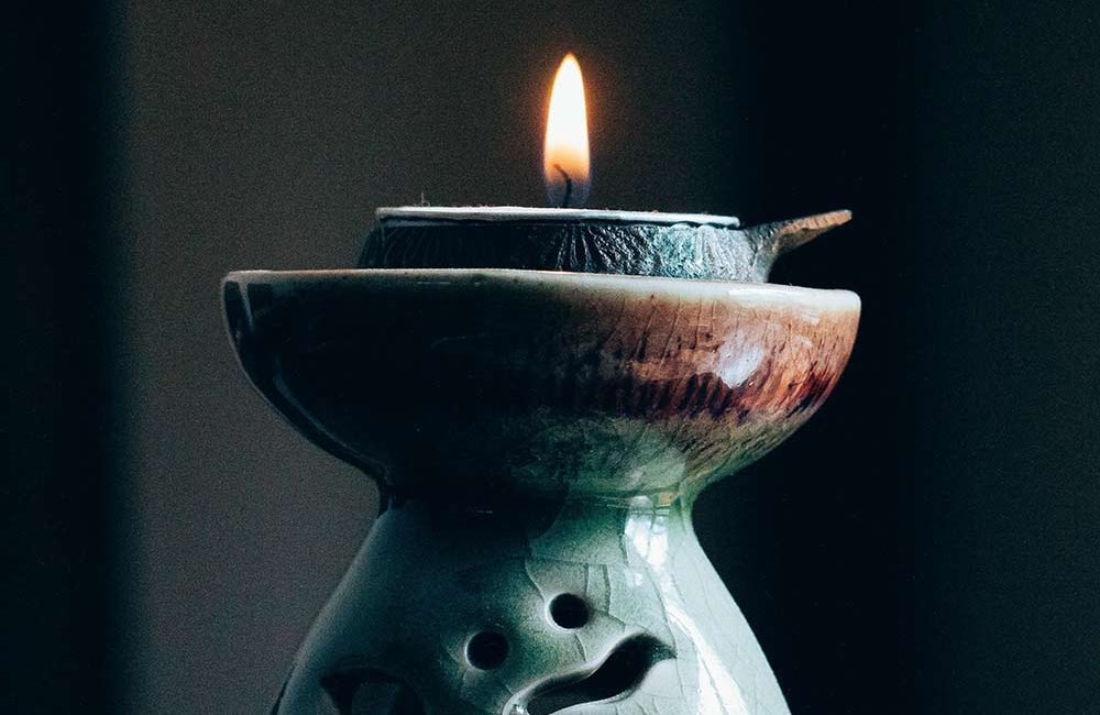 A candle in a green vase with a black background