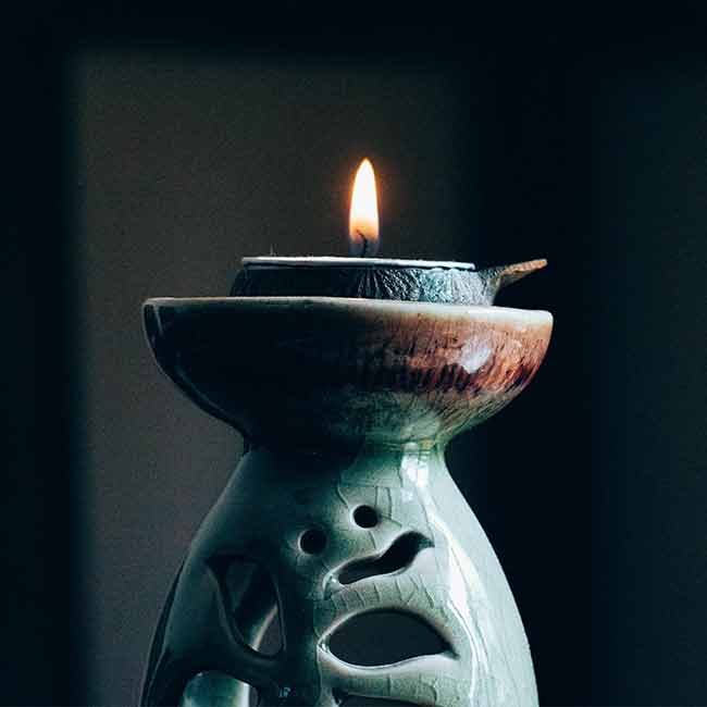 A candle in a green vase with a face on it.